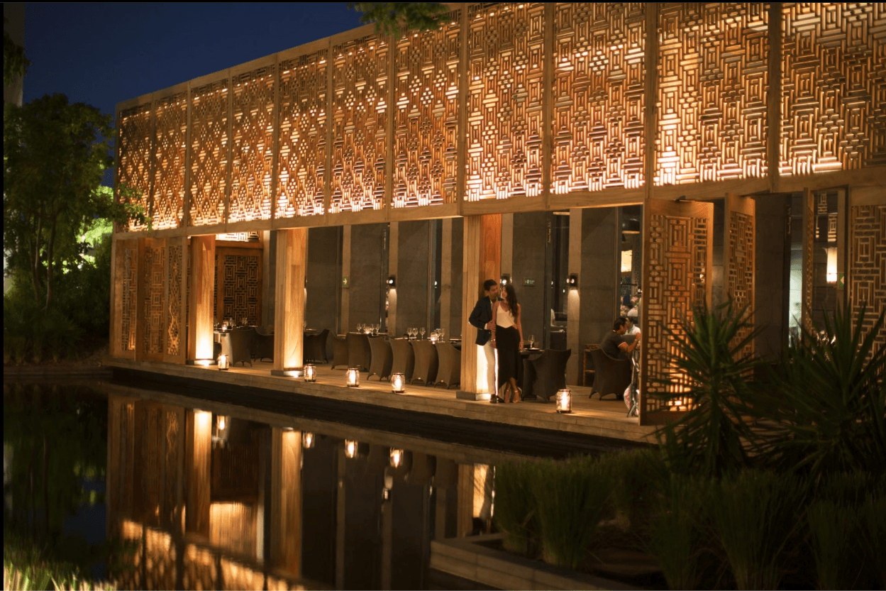 Restaurante iluminado tras una celosía de madera, reflejado en el agua