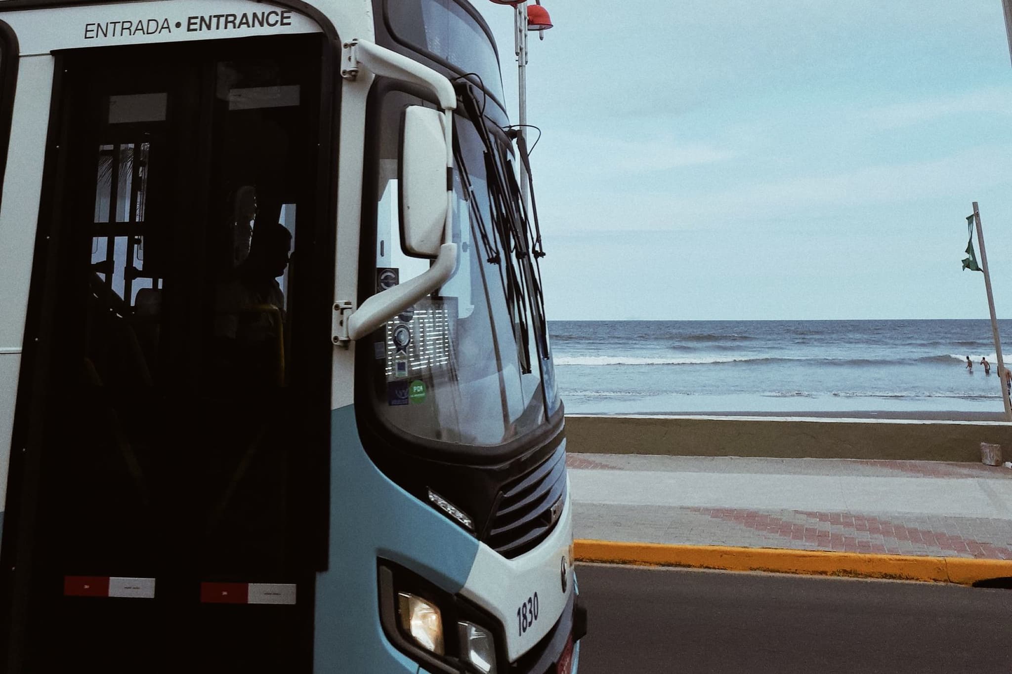 Autobús foráneo estacionado junto al mar, con la puerta marcada Entrada