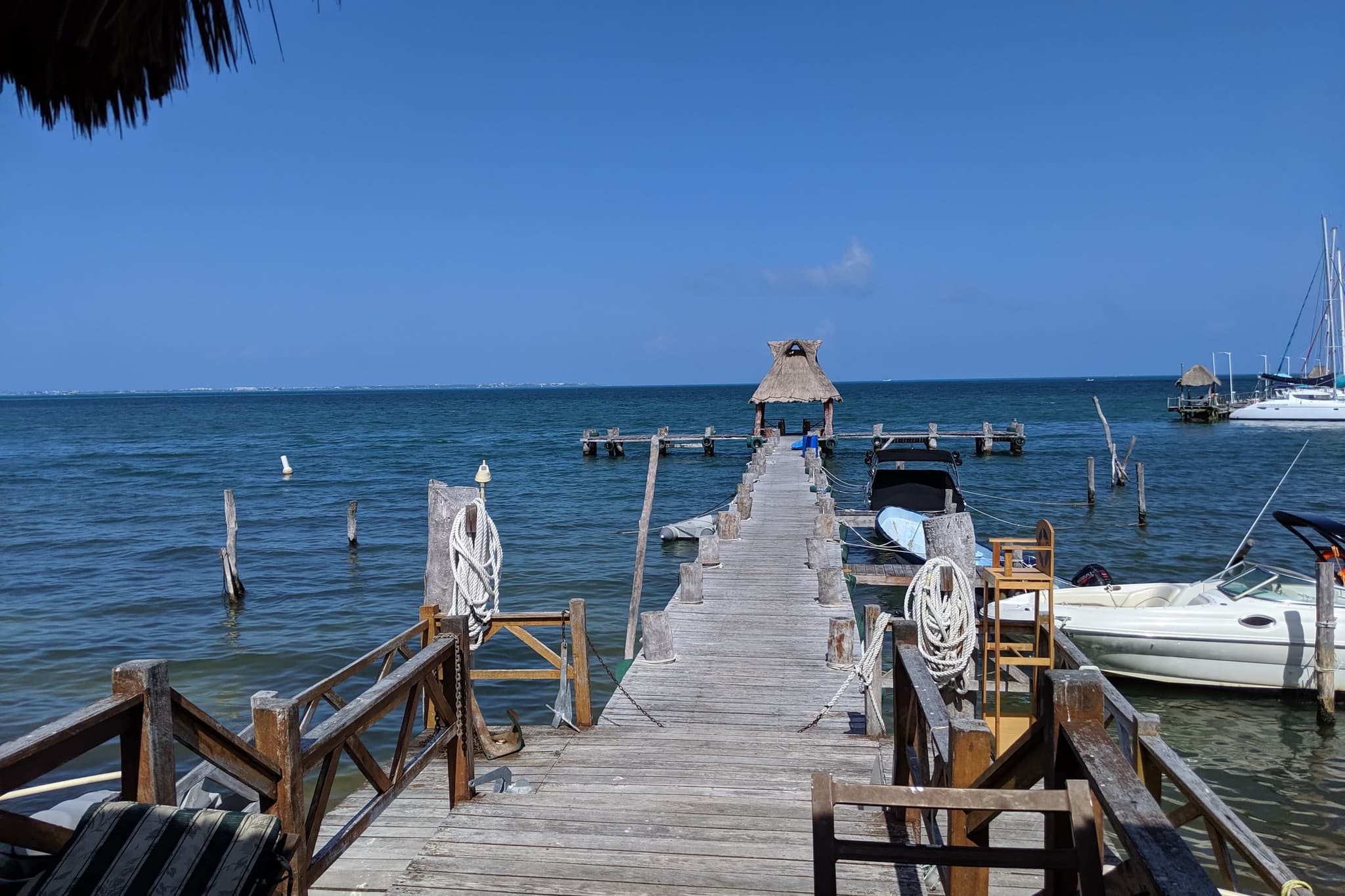 Muelle de madera sobre el mar, con lanchas amarradas y una palapa al final