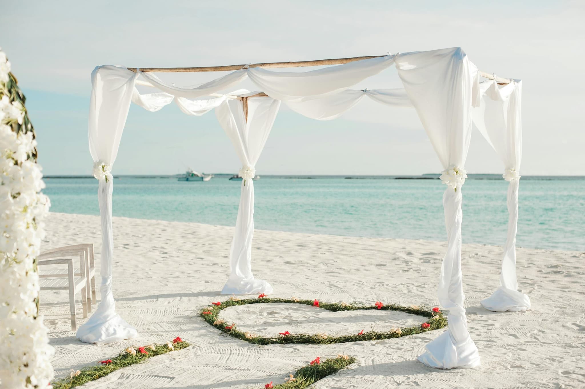 Arco de boda con telas blancas en la arena, frente al mar turquesa