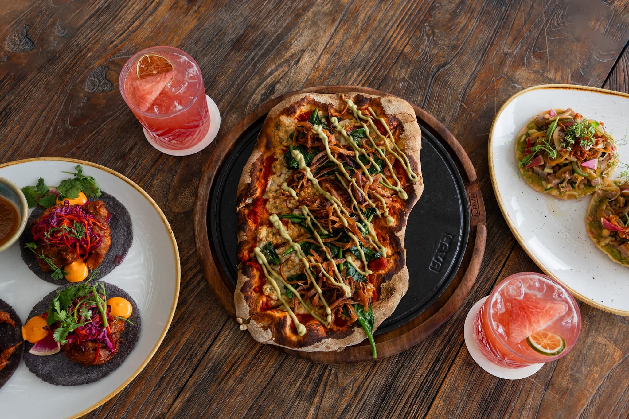 Pizza de leña, tostadas y cócteles servidos sobre una mesa de madera