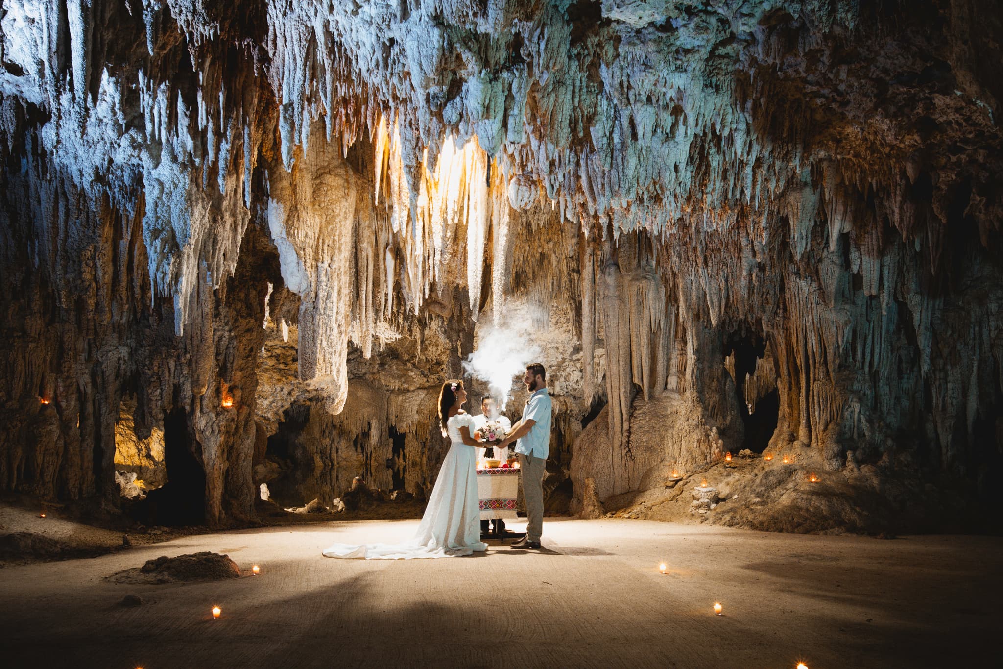 Pareja tomada de la mano durante una ceremonia en una caverna iluminada con velas, bajo miles de estalactitas