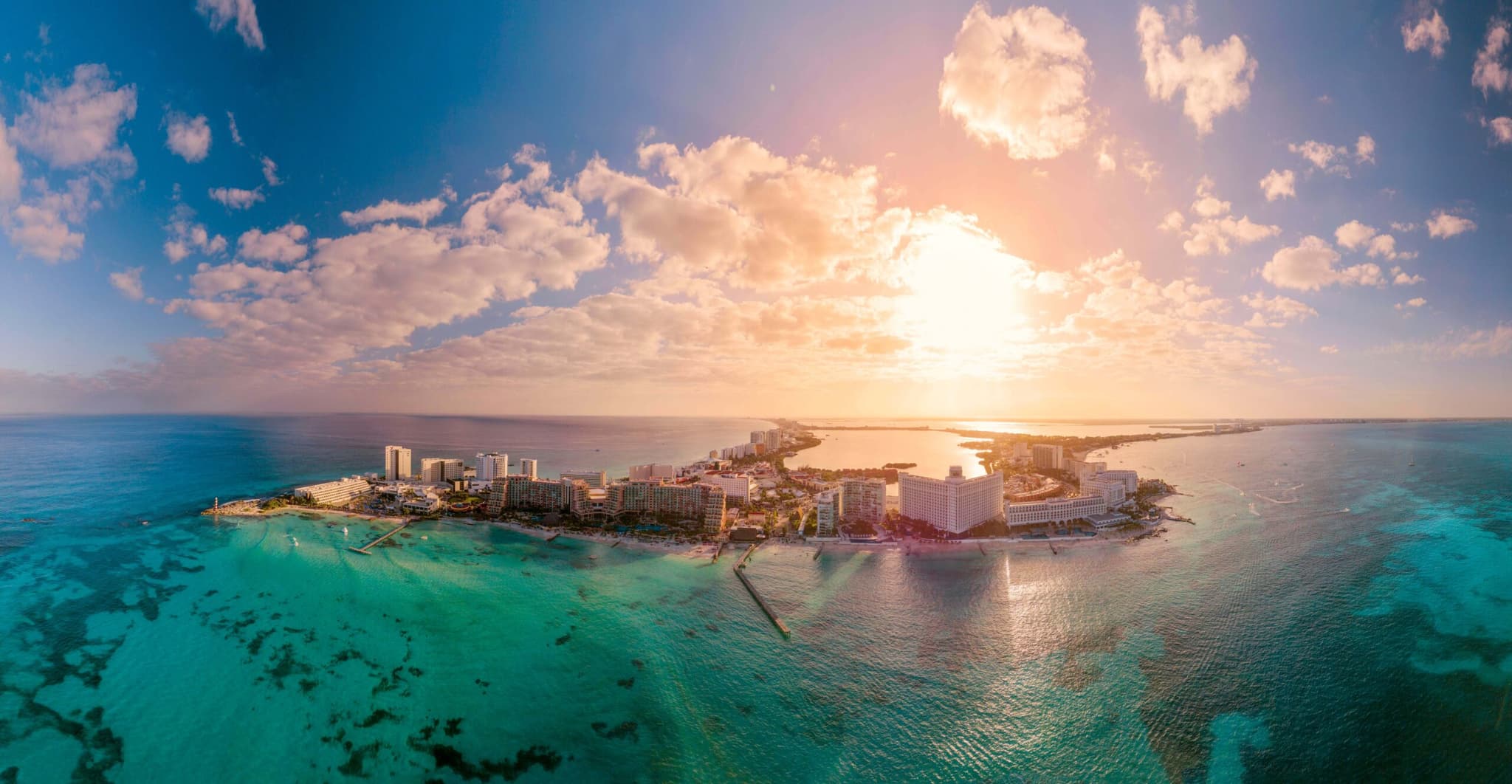 Vista aérea de la Zona Hotelera de Cancún al atardecer, con el sol sobre el mar